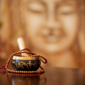 A small dish with prayer beads sitting on it in front of an out of focus picture of the Bhuddha