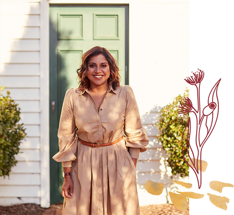 Debanjali is standing in front of a green door and smiling, she is wearing a sand coloured dress